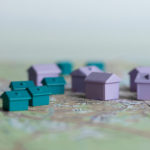 Lila och blågröna monopolhus i olika storlekar utplacerade på en textlös karta.